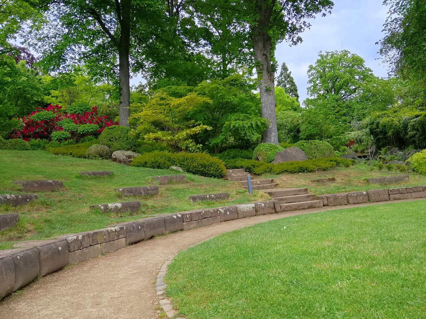 A curved dirt path bordered by a low stone edge beside a green lawn