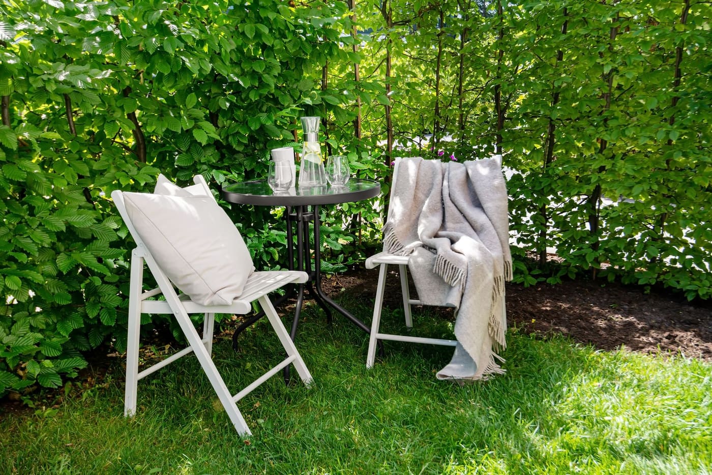 Two chairs and a small round table on a patio with a green hedge behind
